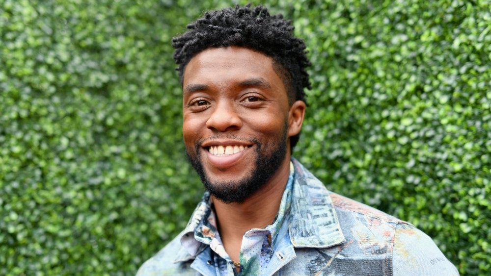 Chadwick Boseman in a multi-colored jean jacket and button-up, smiling outside