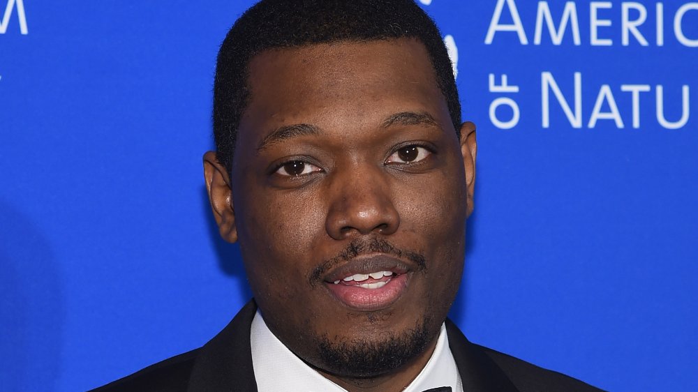 Michael Che in a black tux, posing at a museum event