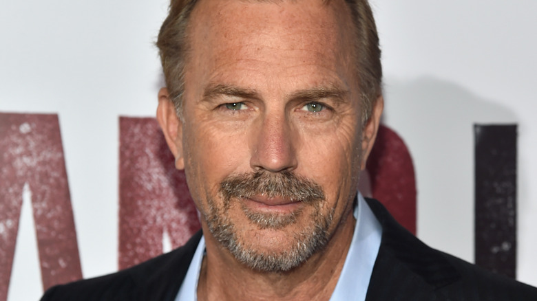 Kevin Costner smiles in a dark suit.